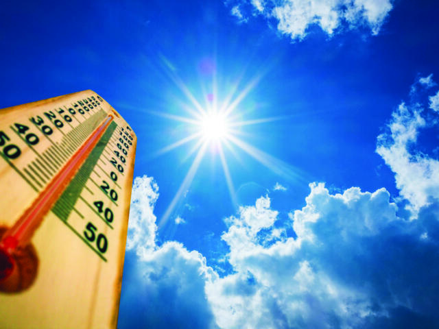 Thermometer in the lower-left foreground with a clear, radiant sun and blue sky, suggesting very hot weather (around 40–50°C).