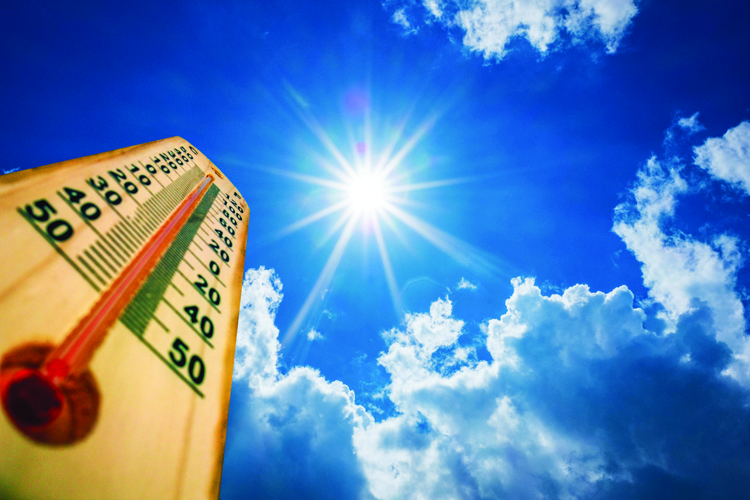 Thermometer in the lower-left foreground with a clear, radiant sun and blue sky, suggesting very hot weather (around 40–50°C).