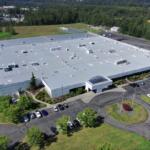Aerial view of a large gray-roofed office/industrial building with a circular driveway and surrounding parking lot.