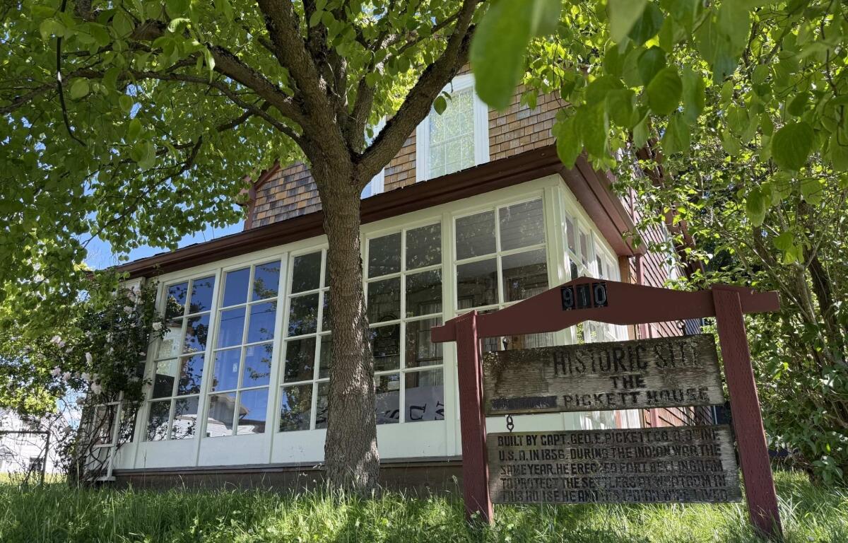 Two-story house with large white-framed windows, shaded by a leafy tree; a weathered sign reads 'Historic Site, The Pickett House'.