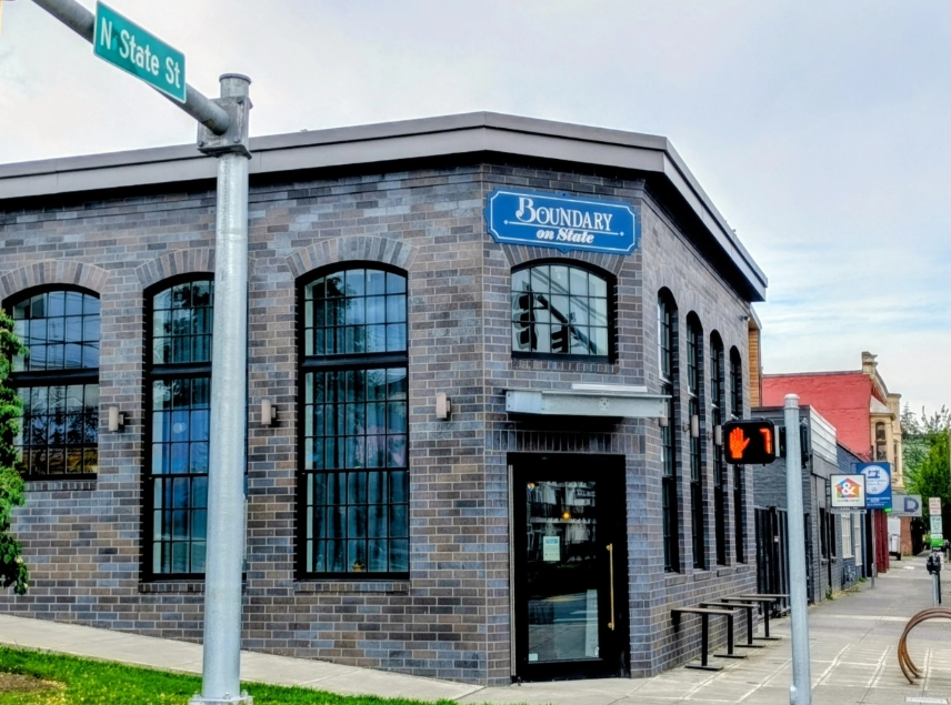 Brick building with large arched windows at a street corner; blue Boundary on State sign above the entrance. Jul set on N State St corner street sign visible.