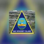 NAS Whidbey Island insignia featuring a blue triangle with yellow border and central crest on a blurred background