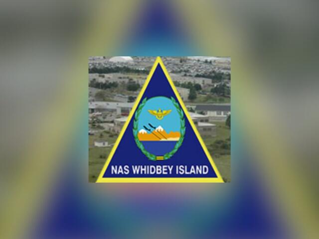 NAS Whidbey Island insignia featuring a blue triangle with yellow border and central crest on a blurred background