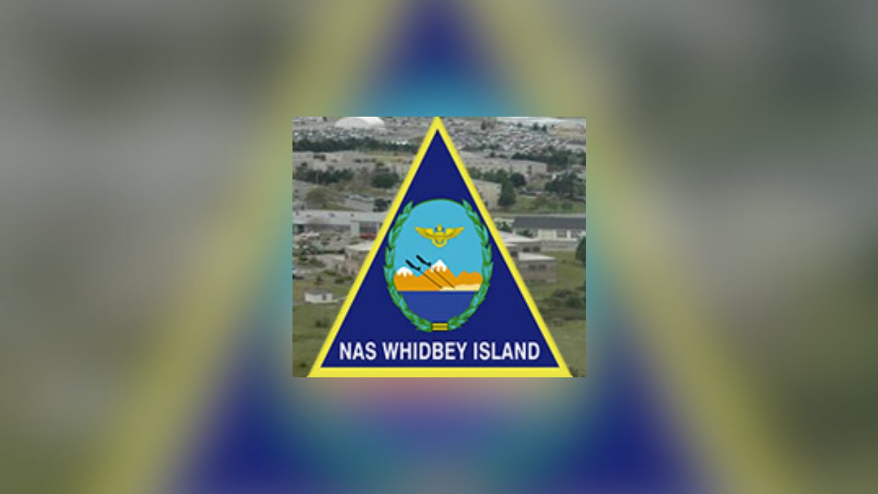 NAS Whidbey Island insignia featuring a blue triangle with yellow border and central crest on a blurred background