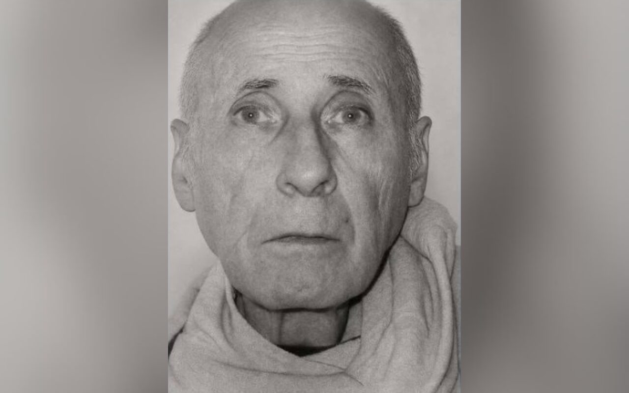 Black-and-white head-and-shoulders portrait of an elderly man with a light scarf around his neck.