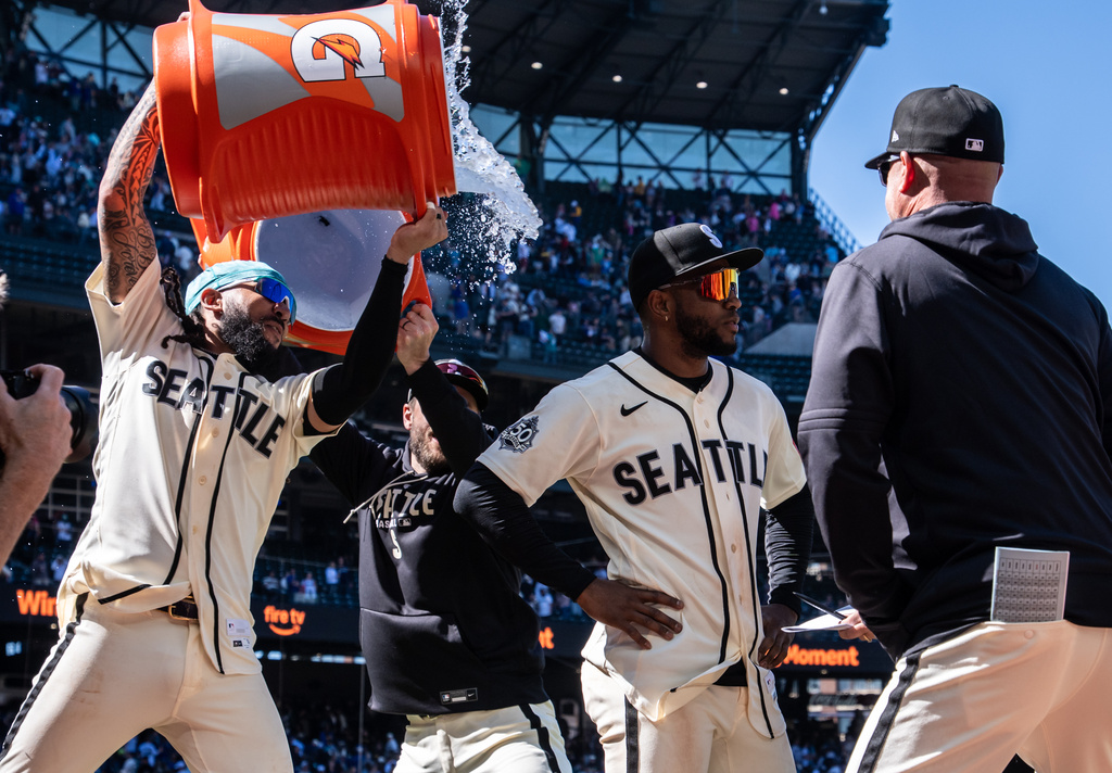 Seattle baseball players celebrate a win as a teammate pours an orange cooler over another player's head on the field,”