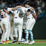 Baseball players in white uniforms huddle together on the field in celebration.