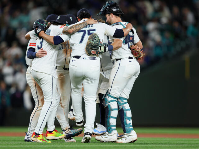 Baseball players in white uniforms huddle together on the field in celebration.