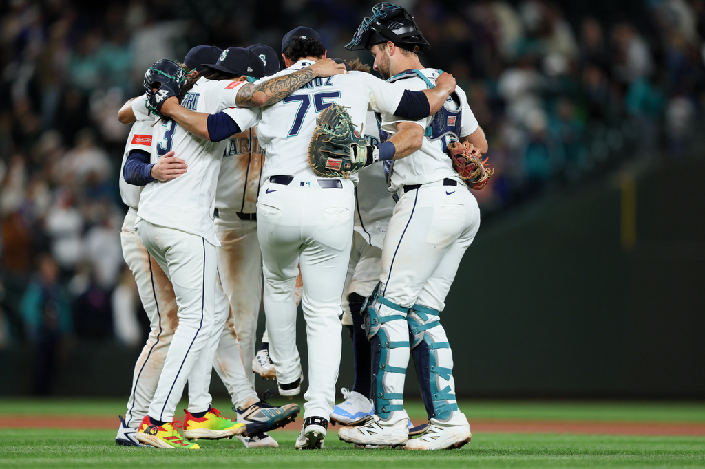 Baseball players in white uniforms huddle together on the field in celebration.