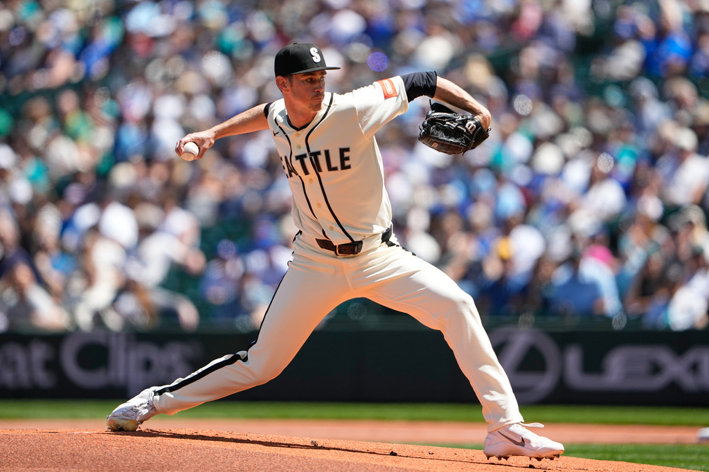 Right-handed pitcher in a beige Seattle jersey delivering a pitch on the mound with a crowded ballpark in the background}