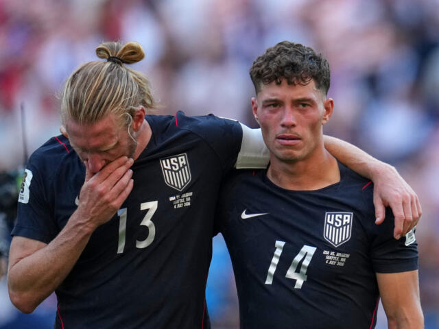 Two USA men’s soccer players with arms around each other after a match, wearing dark uniforms with numbers 13 and 14.
