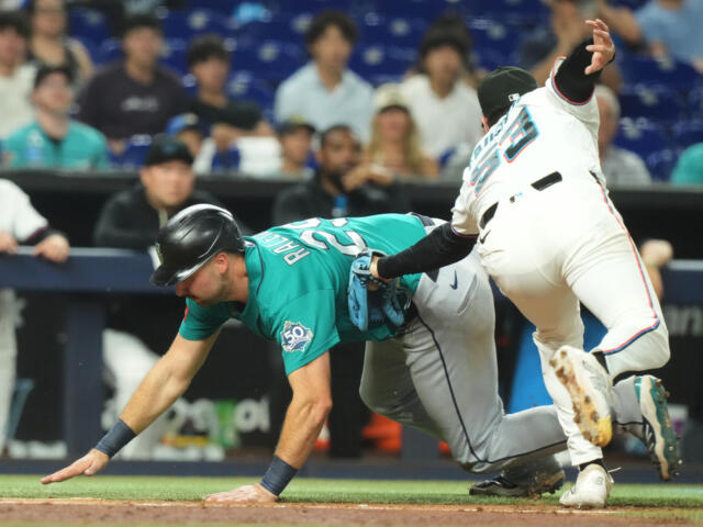 Teal-uniform baserunner slides toward a base while a white-uniform fielder Lunges in to tag the runner.4a9