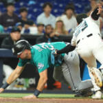 Teal-uniform baserunner slides headfirst toward a base as a white-uniform fielder lunges to tag him.