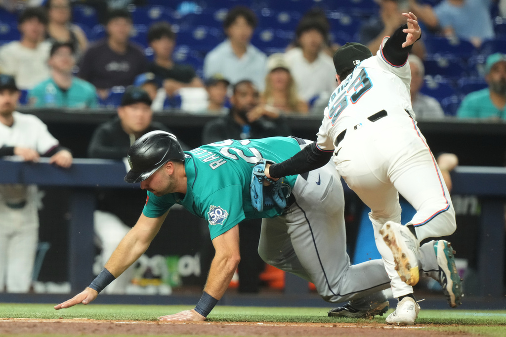 Teal-uniform baserunner slides headfirst toward a base as a white-uniform fielder lunges to tag him.
