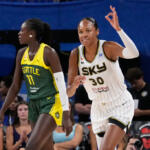 Two female basketball players in motion during a game; white Sky jersey #30 against a Seattle green-yellow jersey defender as spectators watch.