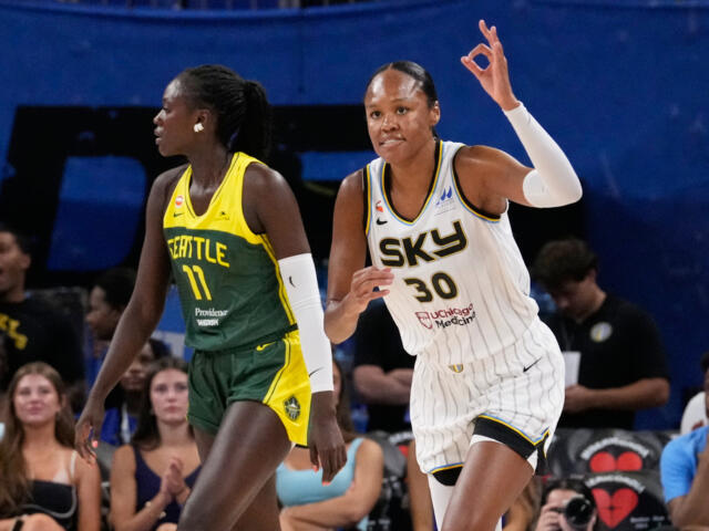 Two female basketball players in motion during a game; white Sky jersey #30 against a Seattle green-yellow jersey defender as spectators watch.