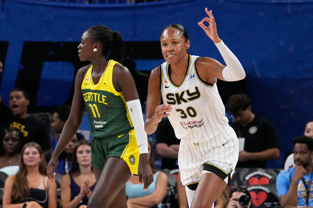 Two female basketball players in motion during a game; white Sky jersey #30 against a Seattle green-yellow jersey defender as spectators watch.