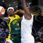 Seattle Storm player (#4) in yellow-green uniform drives with the ball as a defender in white reaches in near the hoop area?
