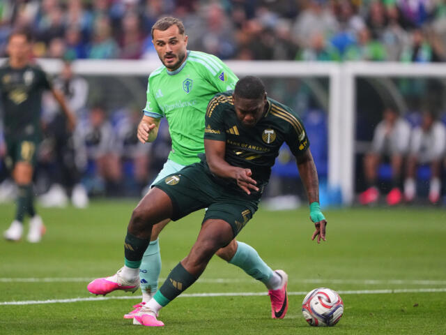 Two soccer players battle for the ball during a match on a green field, with one in a bright green jersey and the other in dark kit close in pursuit.