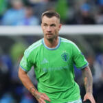 Soccer player in bright green jersey standing on the field, looking focused during a match.