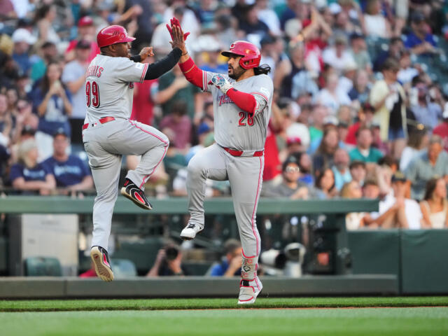 Two baseball players in gray uniforms high-five while jumping on the field as the crowd cheers behind them.