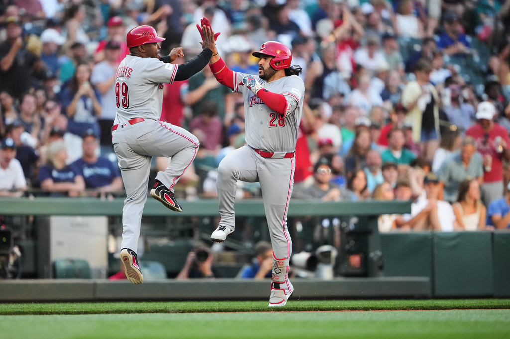 Two baseball players in gray uniforms high-five while jumping on the field as the crowd cheers behind them.