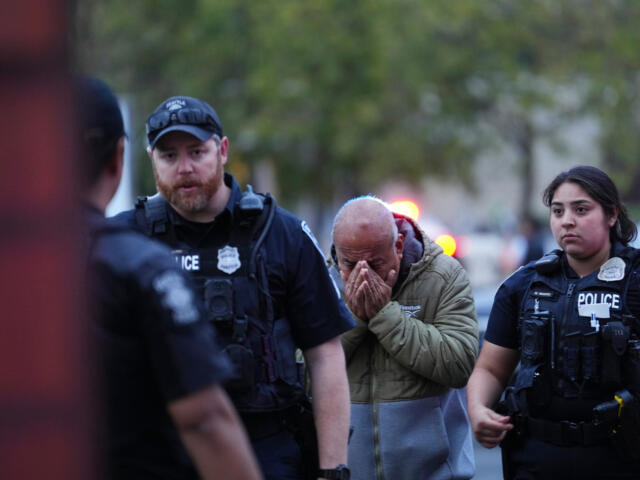 A distressed man with hands covering his face walks between two police officers in tactical vests.