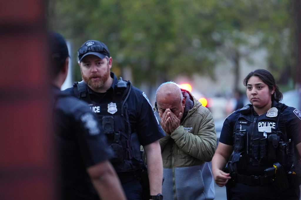 A distressed man with hands covering his face walks between two police officers in tactical vests.