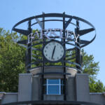 Clock tower structure with a round clock and 'BARKLEY' sign against a blue sky, trees in the background.