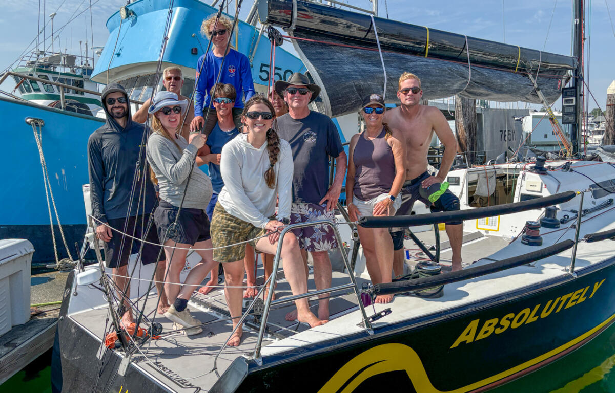 Group of ten people posing on the deck of a sailboat named ABSOLUTELY at a sunny marina.