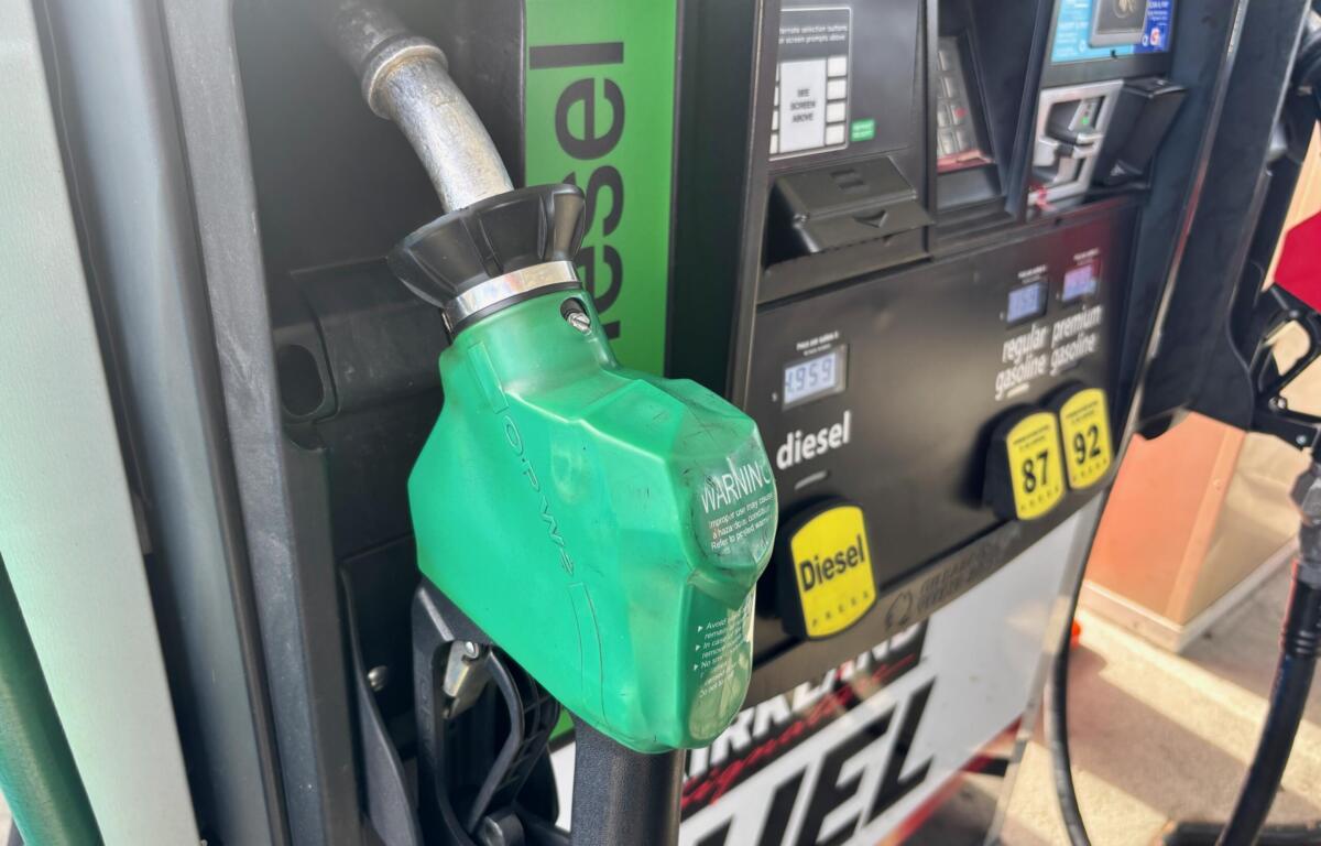 Green diesel fueling nozzle inserted into a gas pump at a station, with digital display and payment panel in the background