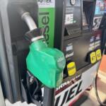Green diesel fueling nozzle inserted into a gas pump at a station, with digital display and payment panel in the background