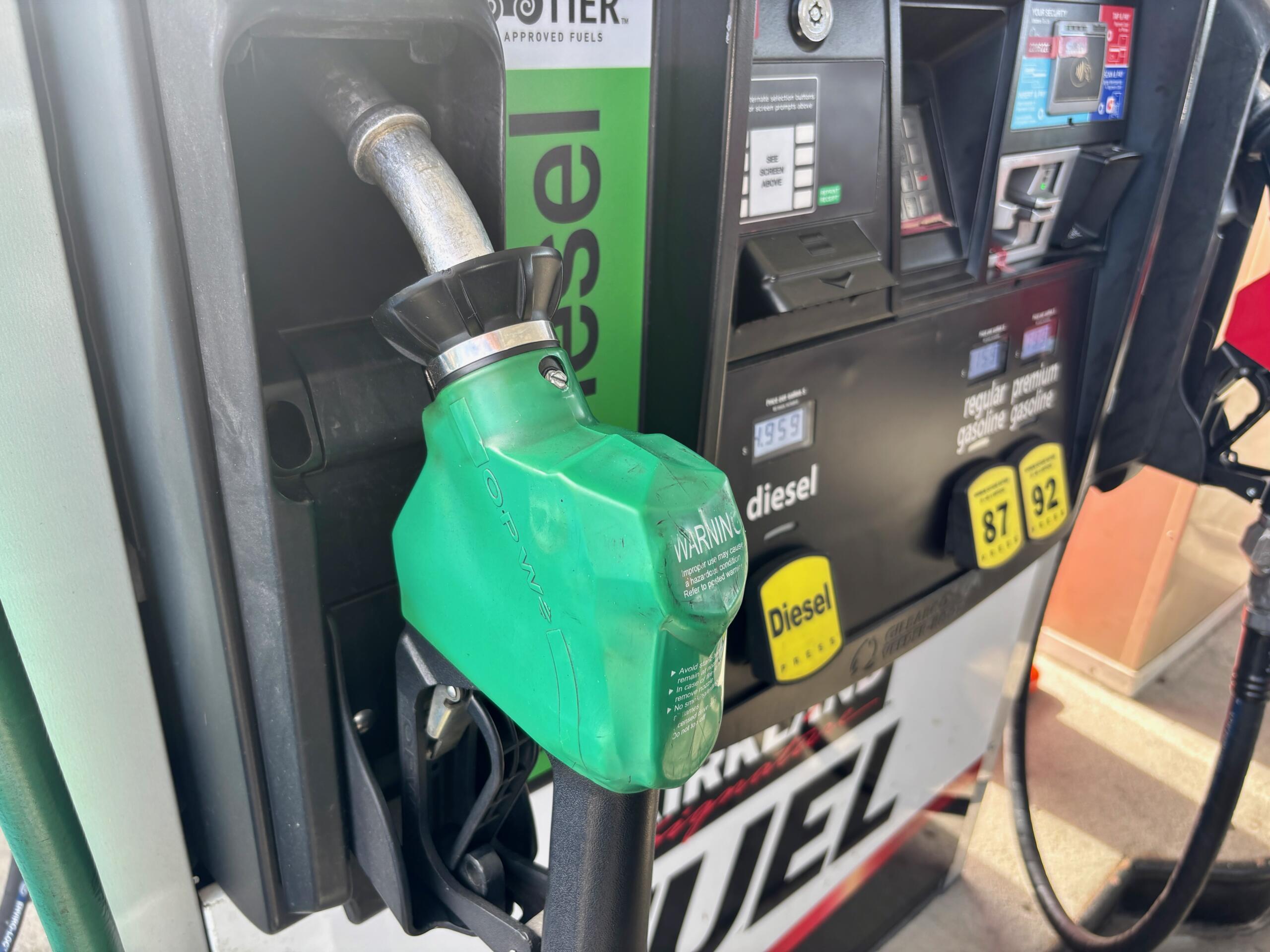 Green diesel fueling nozzle inserted into a gas pump at a station, with digital display and payment panel in the background