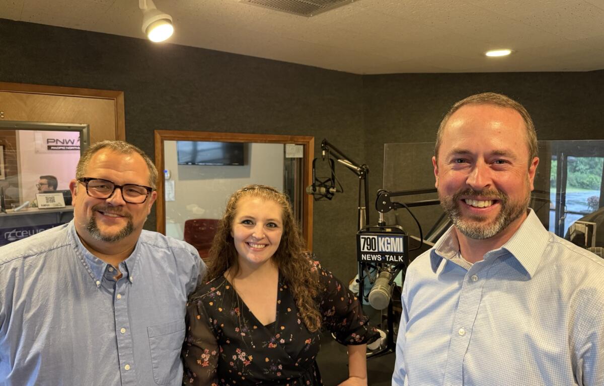 Three radio hosts pose for a selfie in a studio, smiling at the camera beside microphones and a '790 KGMI News Talk' sign on a mic stand.