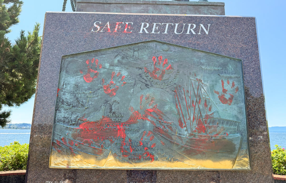 Monument plaque titled Safe Return, a bronze relief with red handprints and a sailing ship, outdoors by the water.