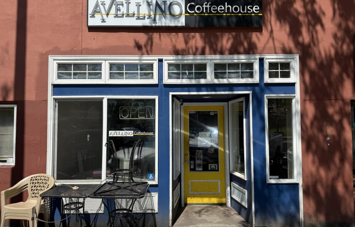 Front of Avellino Coffeehouse with blue storefront trim, yellow door, and outdoor metal tables and chairs under a tree-shadowed wall.