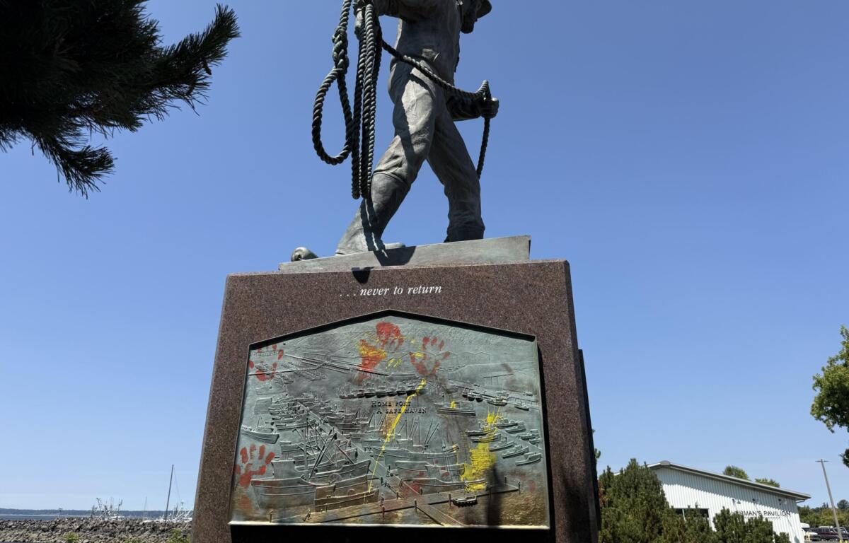 Bronze statue of a person holding a coiled rope atop a tall pedestal, set against a clear blue sky; plaque below features a textured relief with colorful markings and the inscription 'never to return'.