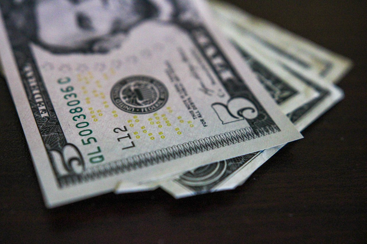 Close-up of several US five-dollar bills fanned on a dark surface with the Lincoln portrait area and serials visible on the front edge.