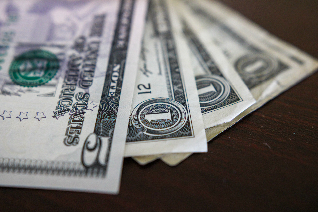 Fanned stack of US one-dollar bills on a dark wooden surface, showing the dollar sign and serials surrounding the front edges.