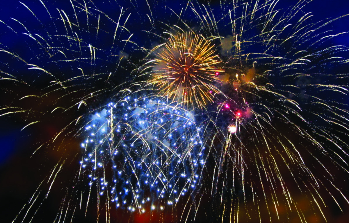 Fireworks bursting in a dark blue night sky with golden streaks and blue sparks radiating outward.