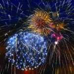 Fireworks bursting in a dark blue night sky with golden streaks and blue sparks radiating outward.