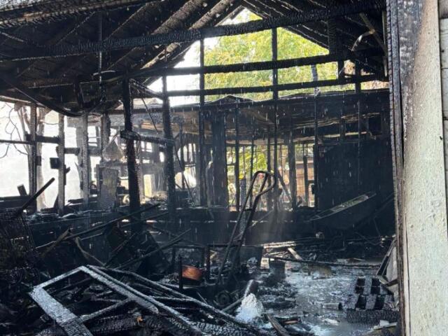 Charred interior of a burned building with blackened beams, scattered debris, and lingering smoke