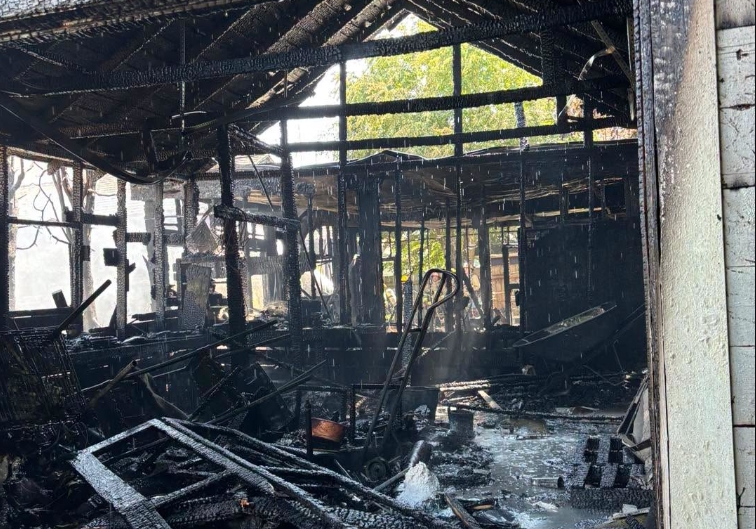 Charred interior of a burned building with blackened beams, scattered debris, and lingering smoke