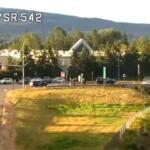 Traffic camera view of I-5 at Sunset Dr/SR 542 showing cars on the highway and a grassy embankment with trees and hills in the background.