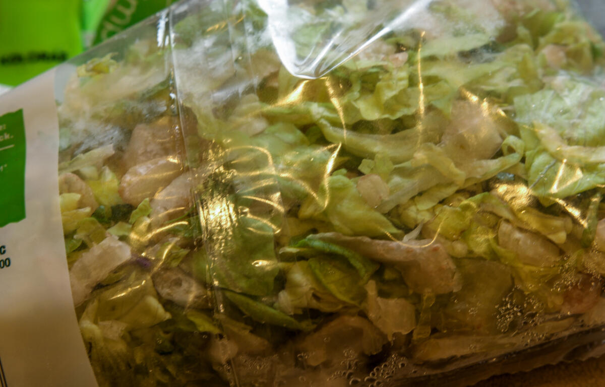 Bag of chopped mixed greens in a clear plastic bag, fresh salad ready for purchase.