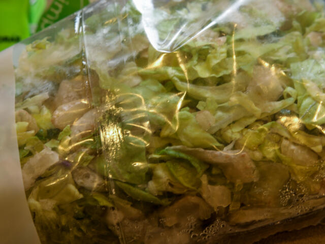 Bag of chopped mixed greens in a clear plastic bag, fresh salad ready for purchase.