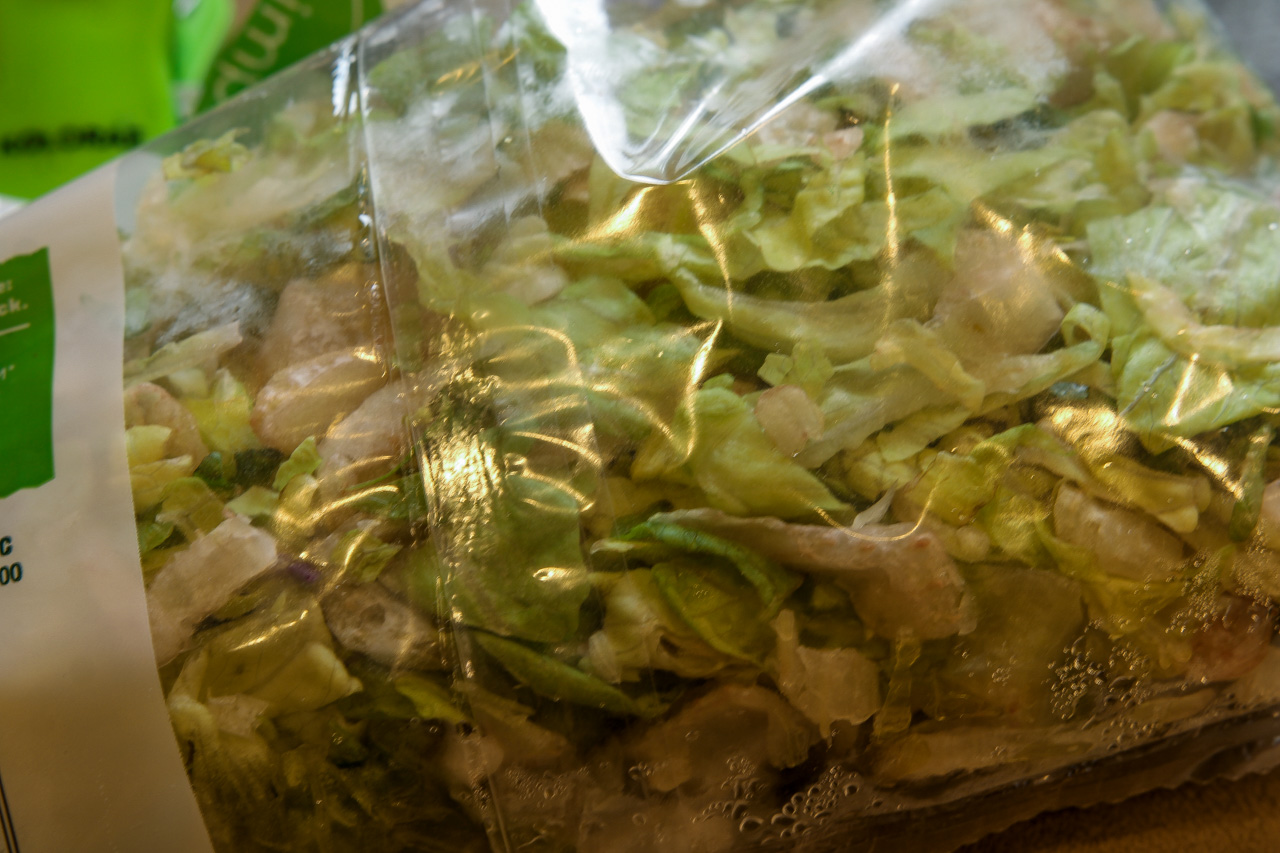 Bag of chopped mixed greens in a clear plastic bag, fresh salad ready for purchase.