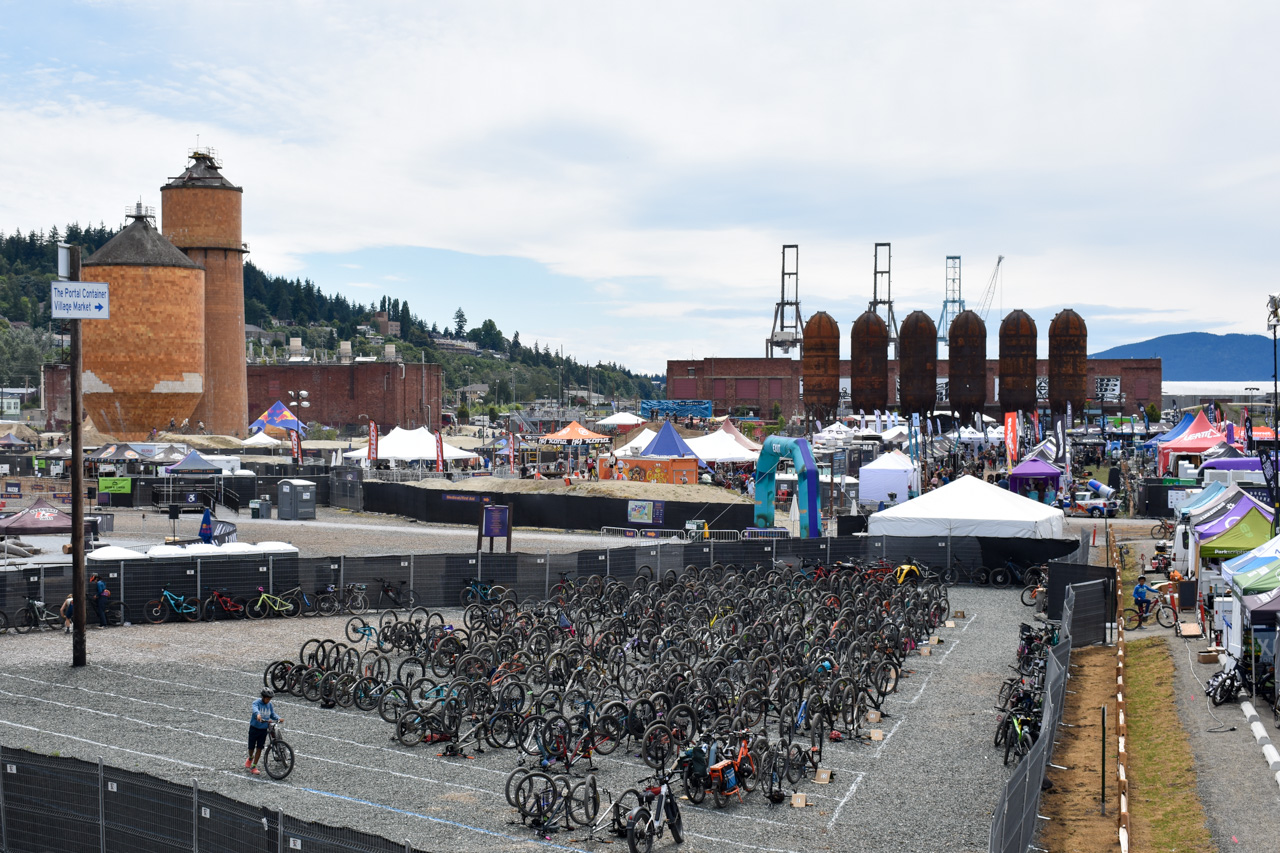 Outdoor bike expo with hundreds of bicycles lined up in front of tents and brick industrial buildings in the background.