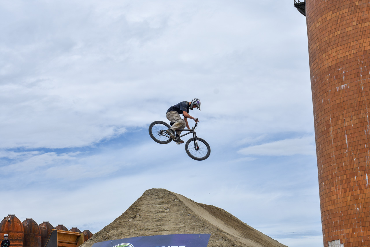 BMX rider in mid-air performing a jump off a dirt ramp against a blue sky.