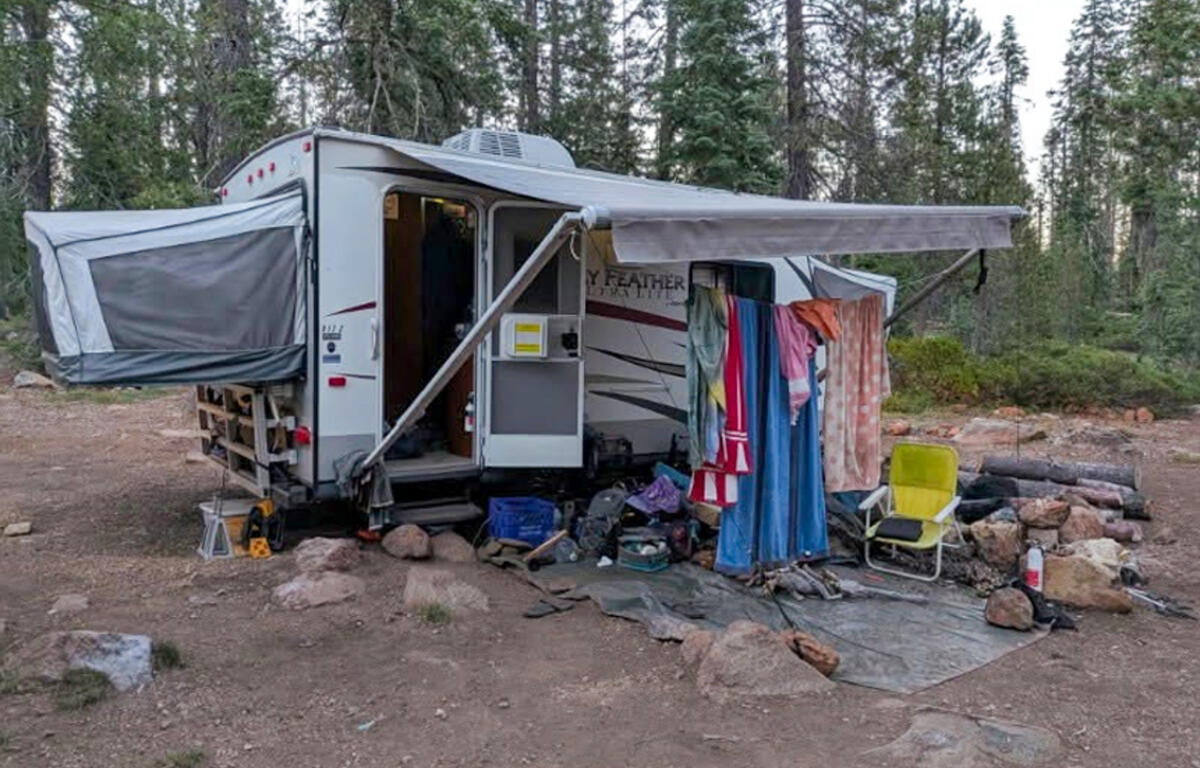 Camper trailer set up in a forest clearing with a clothesline and outdoor seating area under an awning.